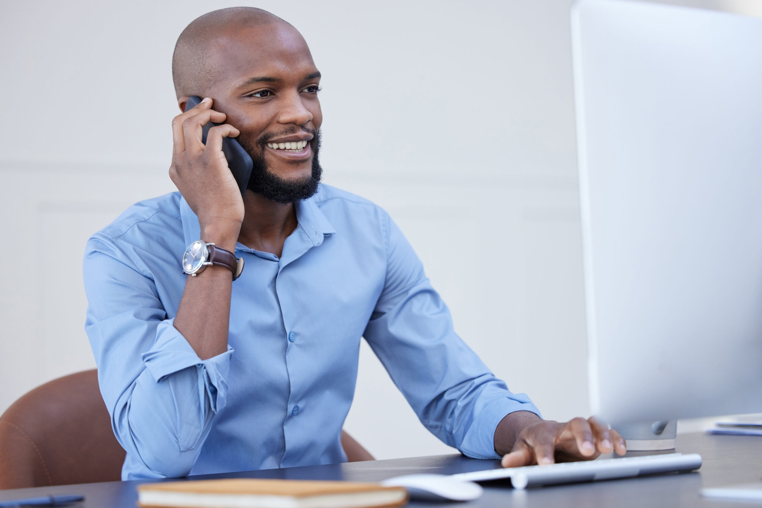 Shot of a young businessman using a computer while on a call at work.